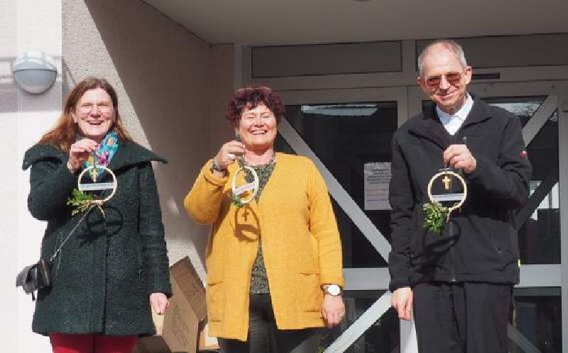 150 Senior*innen erhielten am Palmsonntag eine moderne Interpretation eines Palmbuschens in Form eines mit Grün geschmückten Stickrahmens, an dem ein Holzkreuz befestigt ist. 80 davon überreichten Stadtpfarrer Johann Hofmann (r.) und PGR-Sprecherin Beate Dietrich (l.) der Leiterin des BRK Seniorenwohn- und Pflegeheimes St. Barbara Astrid Geitner (Mitte). - Foto von Werner Schulz