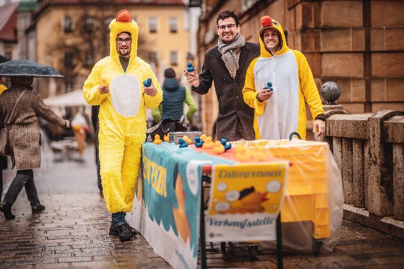 Nicht zu übersehen sind die Verkäufer von Round Table, die bei Wind und Wetter am Verkaufsstand auf der Krambrücke ihre Enten für das große Rennen am Sonntag, 23. April, anbieten. Bild: Michael Golinski/exb - Foto von Uschald