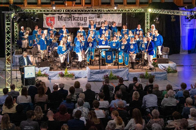 Unter der Konzertüberschrift „Music was my first love“ machte das Orchester des Musikzugs unter Leitung von Marcus Hoffmann (vorne r.) das 38. Osterkonzert zu einem absoluten Highlight des Hirschauer Kulturlebens. Mit im Bild: Vorstand Maximilian Stein (2. Reihe rechts), Nachwuchsorchester Dirigent Erik Remhof (3. Reihe, 4. von rechts) und Moderator Werner Schulz (links am Rednerpult). - Foto von Michael Knietsch
