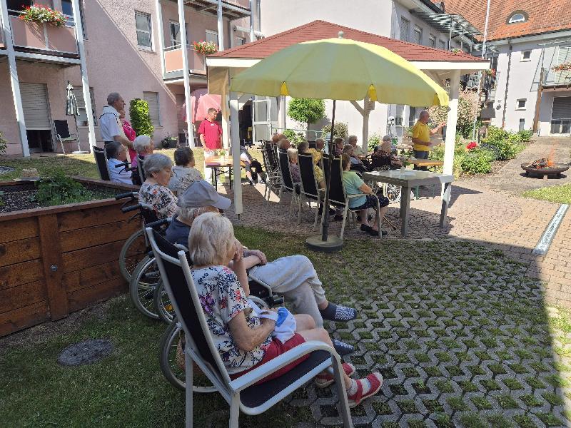 In einem besonderen Rahmen, nämlich verbunden mit einem Johannisfeuer, fand die Bewohnerversammlung des BRK-Seniorenheims St. Barbara statt. Nach dem Bericht des Beiratsvorsitzender Rudi Wild (stehend rechts) segnete Stadtpfarrer Johann Hofmann das Johannisfeuer. Rechts neben ihm (halb verdeckt). Heimleiterin Astrid Geitner. - Foto von Anita Dobmeier